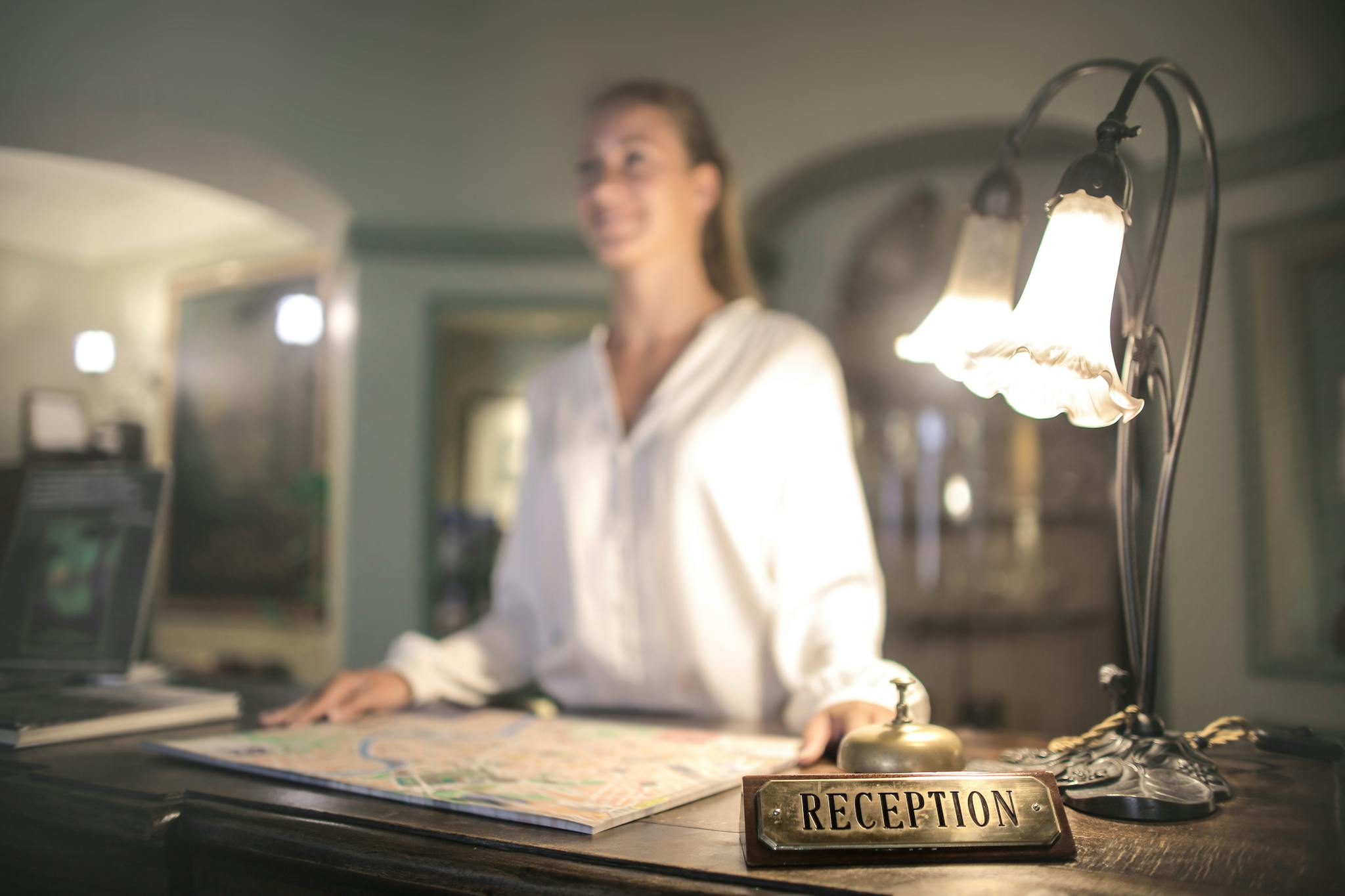 A concierge stands at a hotel reception desk under ambient lighting, ready to assist guests.